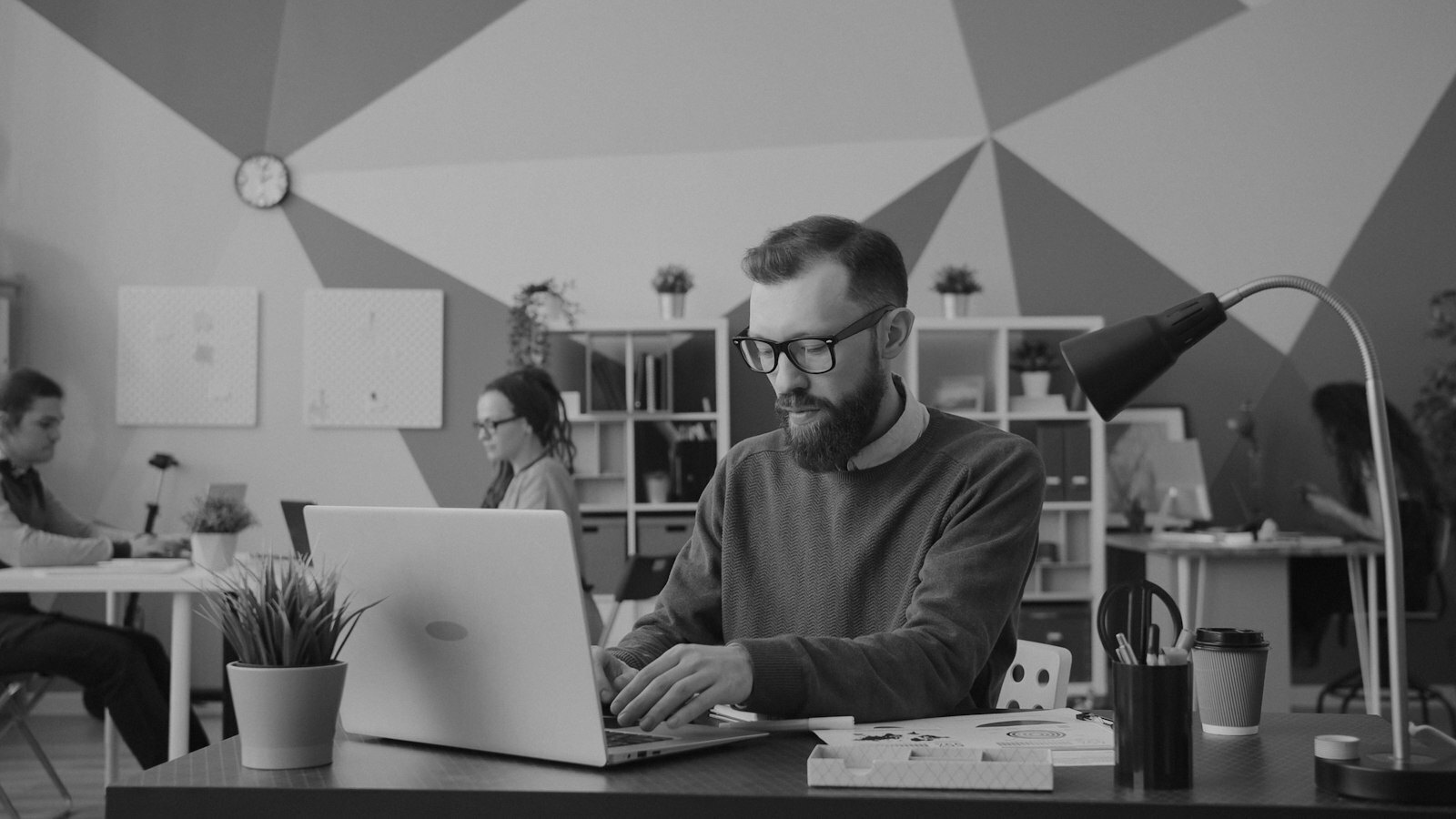 A man with a beard and glasses typing on a laptop in a colorful office