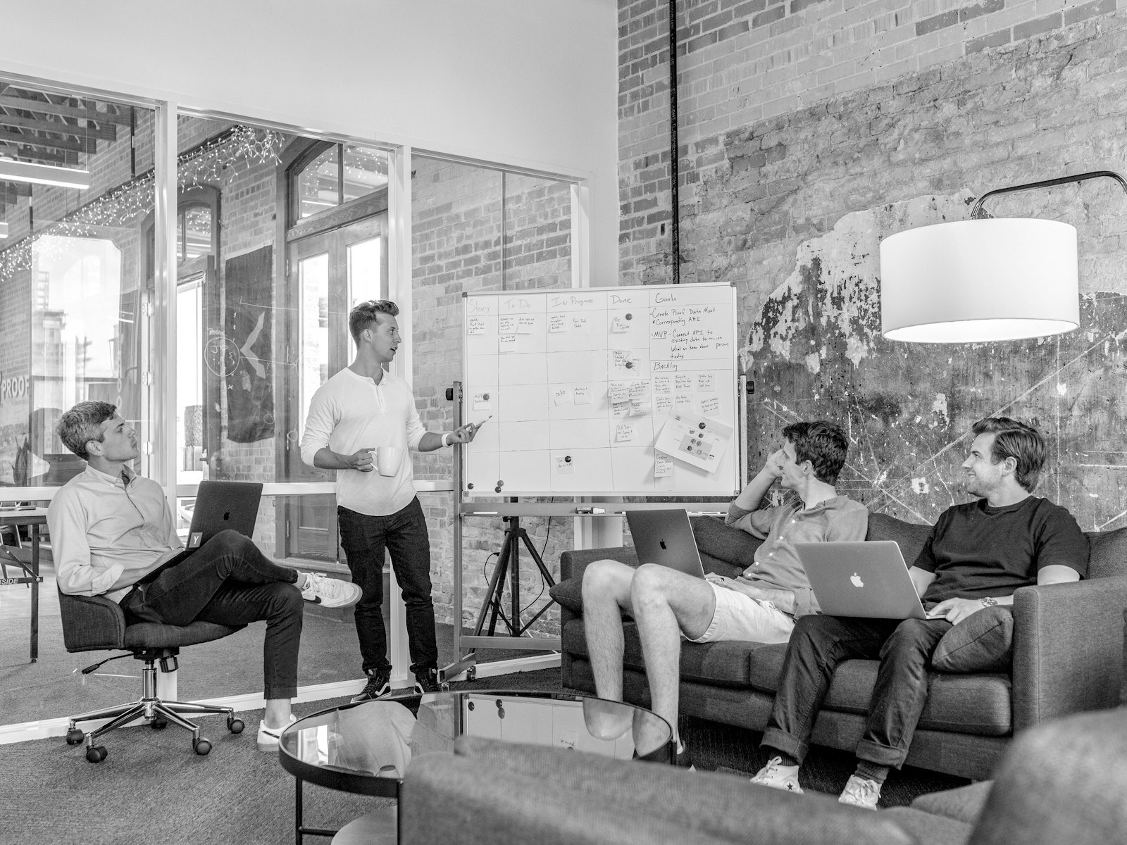 three men sitting while using laptops and watching man beside whiteboard