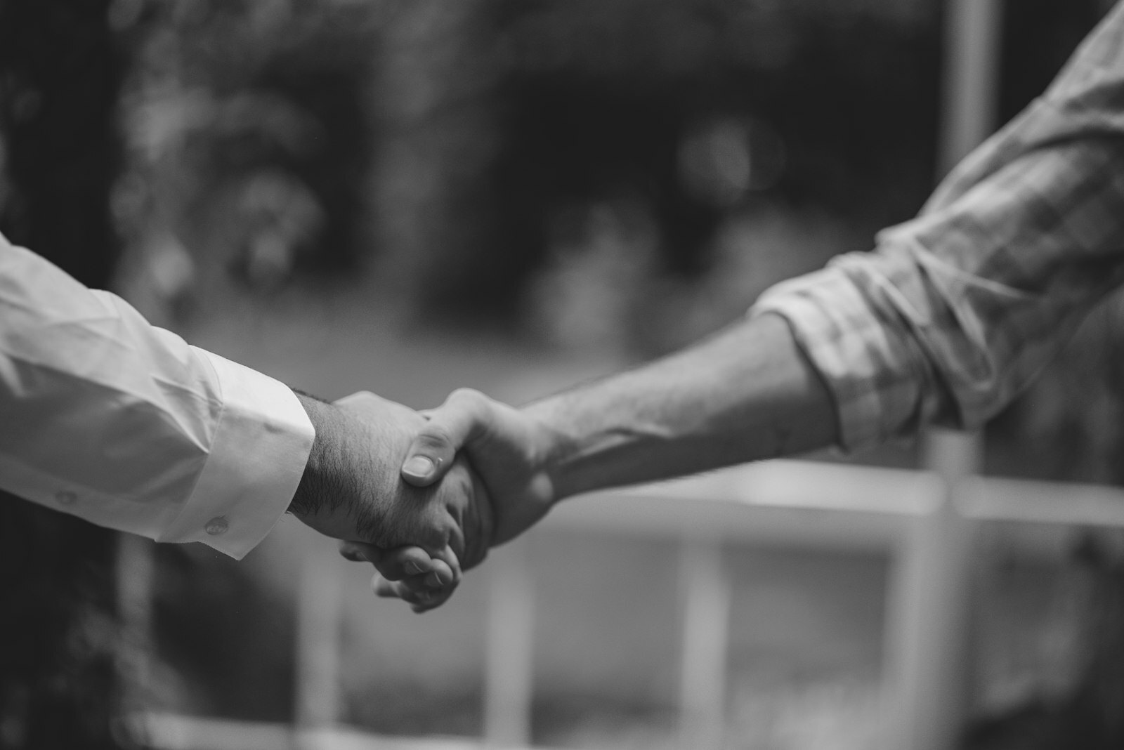 Two people shaking hands in front of a blurred green garden